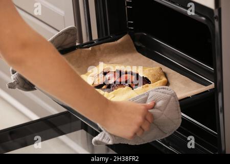 Woman putting uncooked plum galette in oven, closeup Stock Photo