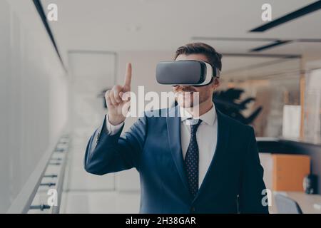 Smiling bearded office employee in suit wearing in VR glasses working in augmented reality in office Stock Photo