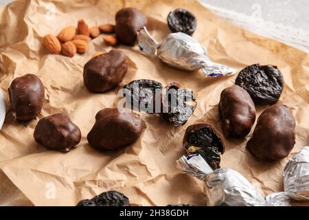Tasty prunes, chocolate candies and almond nuts on parchment, closeup Stock Photo
