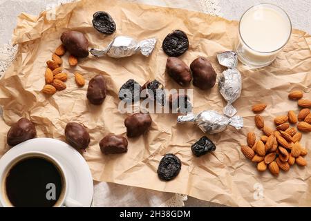Tasty prunes, chocolate candies, almond nuts, glass of milk and cup of coffee on table Stock Photo