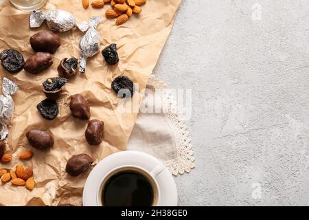 Tasty prunes, chocolate candies, almond nuts and cup of coffee on light table Stock Photo