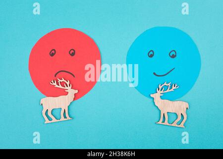 An angry and a smiling face behind two reindeers, customer rating, christmas season, concept, blue background Stock Photo