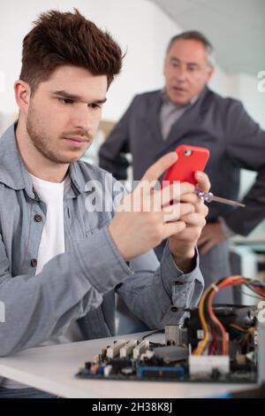 student engineering looking at his smartphone angry teacher in background Stock Photo