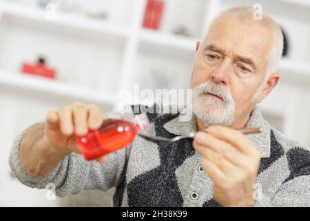 a mature man is pouring cough syrup in a spoon Stock Photo