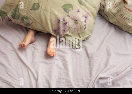 Feet of a small child sticking out from under a blanket with flo Stock Photo