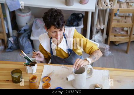 Ceramics workshop owner woman create clay potter in studio decorate dry clay kitchenware with paints Stock Photo