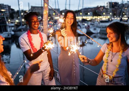 Group of people having fun and celebrating new year night with sparklers on a boat - Happy lifestyle concept - Focus on african man Stock Photo