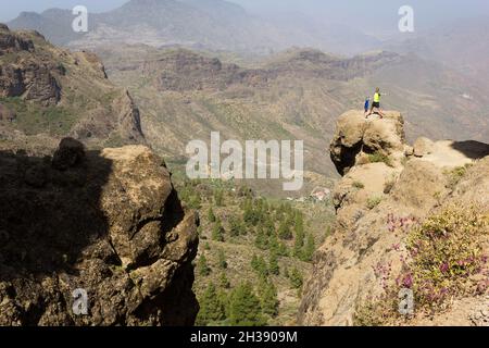 Father and son standing on rock top on sunny day in Roque Nublo, Gran Canaria. Hikers on mountain edge with valley panoramic views. Outdoor activity Stock Photo