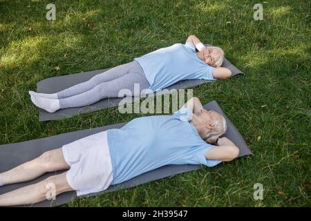 Lovely senior family couple looks at each other lying on mats after training in green park Stock Photo