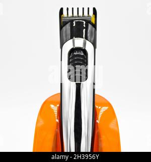 Cordless and chrome electric shaver and orange charger, charged hair clipper isolated on white background Stock Photo