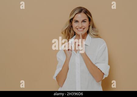 Young cheerful pretty woman holding index finger on lips and making hush gesture Stock Photo