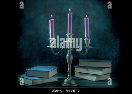 Magic studies. Occult books and purple candles in a vintage candleholder, toned image Stock Photo