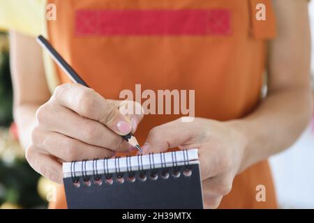 Female waiter writing down ordered dishes in notebook with pencil closeup Stock Photo