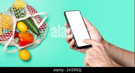 Grocery online background concept. A hand with a smartphone and eco-friendly bag with vegetables and fruit from the supermarket. Order, grocery and delivery food from eco-market. High quality photo Stock Photo