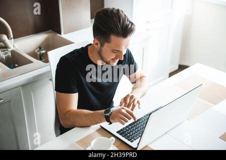 Young man working remotely during a pandemic. Overhead shot sitting at the table in front of the laptop. Busy businessman. Stock Photo