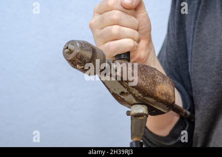 A man holds an old manual drill in his hand. A rusty metal hand tool. Close-up.  Selective focus. Stock Photo