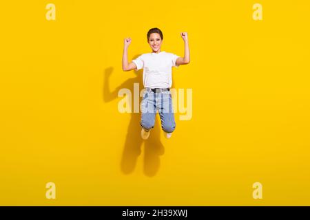 Full size photo of optimistic brown hairdo young lady jump wear white t-shirt jeans isolated on yellow color background Stock Photo