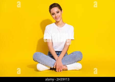Full size photo of nice brown hairdo millennial lady sit wear white t-shirt jeans isolated on yellow color background Stock Photo
