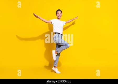 Full size photo of funny brown hairdo young lady stand fly wear white t-shirt jeans isolated on yellow color background Stock Photo