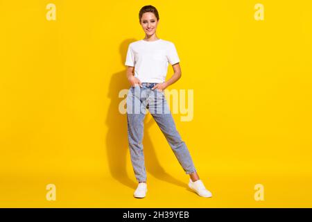 Full size photo of cute brown hairdo young lady stand wear white t-shirt jeans isolated on yellow color background Stock Photo