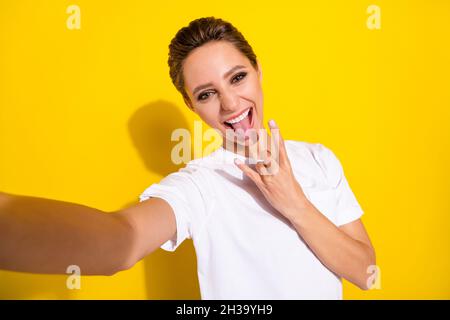 Photo of cool brown short hairdo millennial lady do selfie show rock sign wear white t-shirt isolated on yellow color background Stock Photo