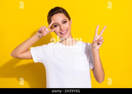 Photo of funky brown short hairdo young lady show v-sign wear white t-shirt isolated on yellow color background Stock Photo