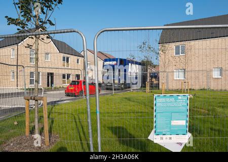 Covid working practice information sign on the fence surrounding the play are next to the houses where new residents are moving in at Keepers Green in Stock Photo