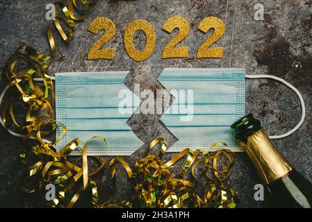 New Years Eve celebration concept background.Protective surgical mask split in two with the numbers 2021 and Champagne bottle on gray background. Conc Stock Photo