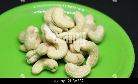 The pile of cashew nuts is on a black background on a green plate Stock Photo