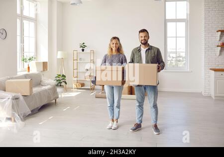 Happy young couple standing in their new house or apartment, holding boxes and smiling Stock Photo