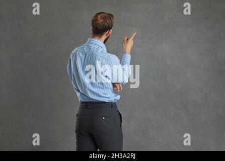 Focused businessman turned his back to the camera standing on a gray background. Stock Photo