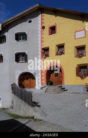 A clear dividing line between two large traditional Engadiner family houses separates colour schemes of honey gold and salmon pink and grey set off by white in the historic Romansh-speaking village of Ardez in the lower Engadine Valley, Graubünden or Grisons canton, eastern Switzerland. Stock Photo