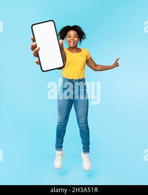 Great new mobile app. Excited African American woman jumping and showing smartphone with blank screen, mockup Stock Photo
