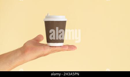 Man's hand holding brown paper coffee cup with white plastic cap on beige background with copy space Stock Photo