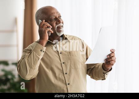 Senior African American Businessman Talking On Cellphone Holding Paper Indoors Stock Photo