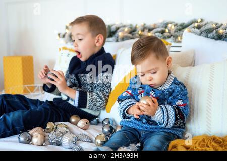 Focus on cute little baby examines a Christmas toy in his hands. Older brother is fooling around in the background. Christmas or New Year's mood. Love Stock Photo