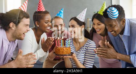Closeup portrait of happy friends in party hats celebrating birthday with cake Stock Photo