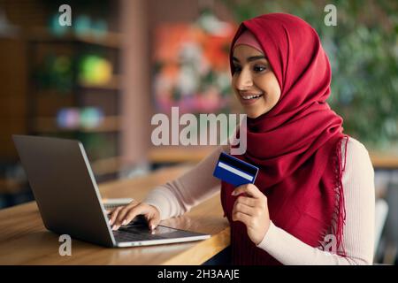 Arabic lady holding credit card, using laptop at cafe Stock Photo