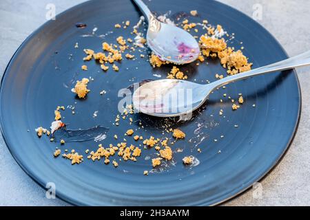 Empty dark plate with crumbs and dirty spoon on a table after sweet pie. Stock Photo