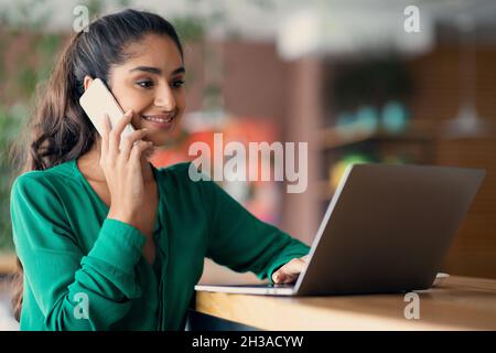 Successful arabic woman working online, having phone conversation, copy space Stock Photo