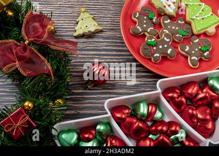 Sugar coated biscuits and Christmas theme cookies on a red ceramic plate with a plate of chocolate candies and Christmas ornaments. Stock Photo