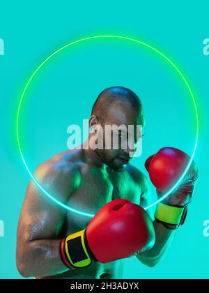 Creative artwork of prfessional male boxer in motion over neon geometric element isolated over green background Stock Photo