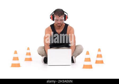 Constructor man working with a laptop within a delimited area with orange cones Stock Photo