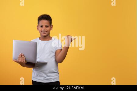 Cheerful black boy with laptop pointing at copy space Stock Photo