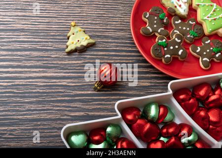 Sugar coated biscuits and Christmas theme cookies on a red ceramic plate with a plate of chocolate candies and Christmas ornaments. Stock Photo