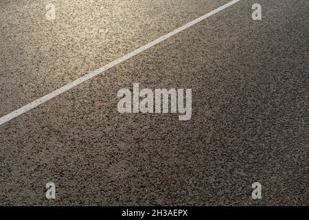 The texture of a new asphalt road with a dividing white stripe on a sunny morning Stock Photo
