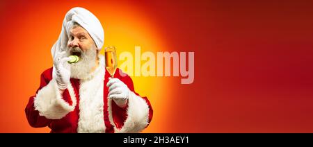 Funny senior man wearing white towl and costume of Santa Claus congrats everybody with New Year 2022 isolated on red yellow background in neon. Stock Photo