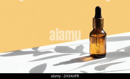 Dropper glass bottle mockup on geometric yellow and white gray concrete background with hard shadows from plants. Hard shadows. Creative cosmetic back Stock Photo
