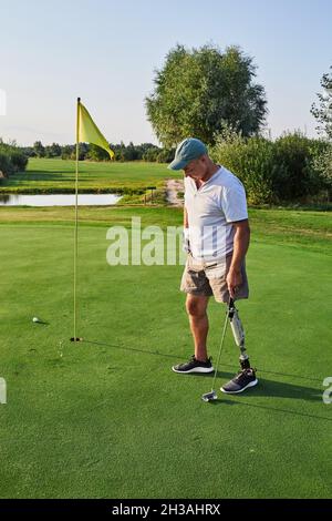 Adult man with a artificial leg playing golf outdoor at green golf course and lives a full life. Golf for people with disabilities Stock Photo