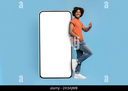 Handsome african american hipster leaning on big cellphone, mockup Stock Photo